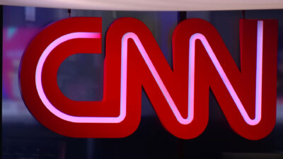 Logotipo tridimensional da CNN Brasil em cor vermelha com iluminação interna branca instalado em uma parede da redação