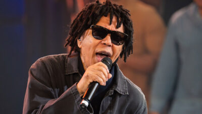 O cantor Djavan com seus dreadlocks e óculos escuros canta durante apresentação no programa Altas Horas, da TV Globo, segurando microfone