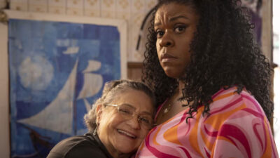 Dona Oliveira (Fafy Siqueira) sorri abraçada em Neide (Cacau Protásio), que a olha desconfiada em cena do filme A Sogra Perfeita 2