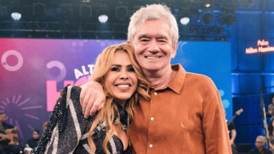 Joelma e Serginho Groisman sorriem abraçados no palco do Altas Horas com telão colorido ao fundo durante gravação na TV Globo