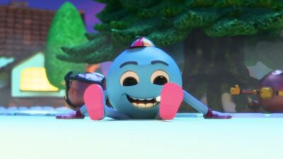 Personagem azul e redondo da animação Marry em: Um Pedido Especial sorri sentado na neve usando boné de hélice colorido e sapatos rosas com árvores ao fundo