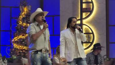 Maurício e Mauri cantam no palco do programa Aparecida Sertaneja com árvore de Natal ao fundo e cenografia iluminada na TV Aparecida