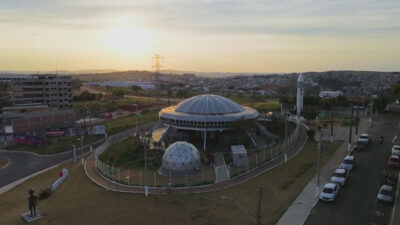Memorial do ET com formato de disco voador visto do alto ao entardecer em cena da série O Mistério de Varginha da TV Globo