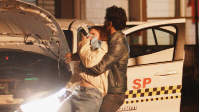 Paula (Débora Ozório) e Roberto (Ruan Aguiar) ao lado de táxi com o capô aberto em cena da novela Tudo por Uma Segunda Chance