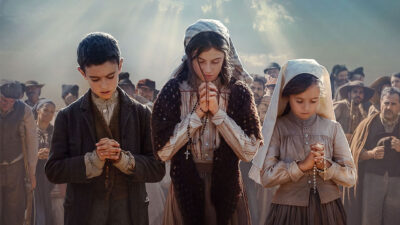 Cena do filme Fátima A História de um Milagre mostra multidão de fiéis em campo aberto olhando para o céu iluminado em Portugal
