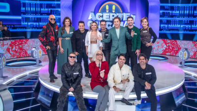 Tom Cavalcante de terno verde sorri ao lado de diversos participantes no palco iluminado do programa Acerte ou Caia! na Record