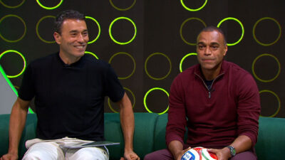 André Rizek sorri e Denílson de casaco vinho segura bola sentados no sofá verde do cenário do programa Fechamento no canal SporTV