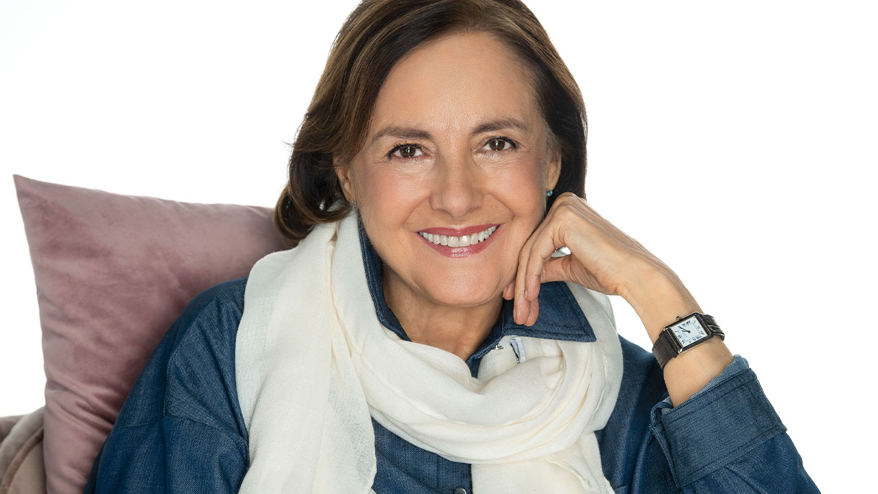 Catarina (Diana Bracho) sorri com a mão no queixo, camisa jeans e lenço branco em foto promocional da novela Presente de Amor
