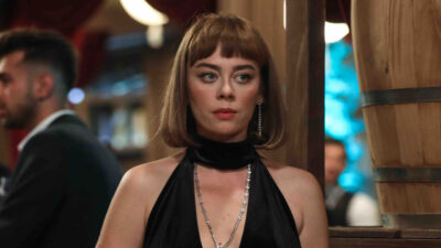 Demet Evgar como Cemre Kayabeyli em cena da novela Chamas do Destino veste vestido preto com colar de brilhantes em ambiente festivo