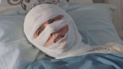 Hazar Erguclu como Cicek deitada com rosto enfaixado e expressão de dor em cama de hospital na novela turca Chamas do Destino