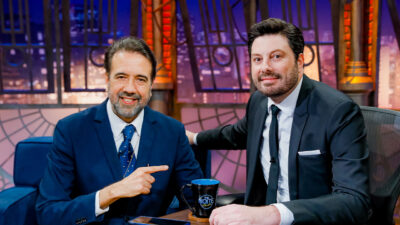 Danilo Gentili e Jorge Lordello sentados lado a lado no estúdio do The Noite com caneca do programa sobre a mesa