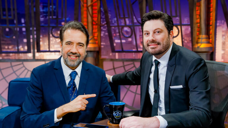 Danilo Gentili e Jorge Lordello sentados lado a lado no estúdio do The Noite com caneca do programa sobre a mesa