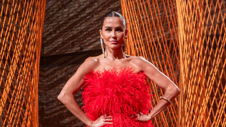 Deborah Secco posa com vestido tomara que caia de plumas vermelhas e brincos longos durante gravação do reality Terceira Metade
