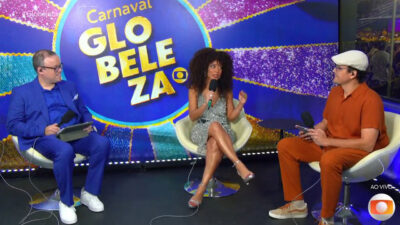 Everaldo Marques, Valéria Almeida e Judson Sales conversam sentados em estúdio do Carnaval Globeleza com microfones e painel colorido ao fundo