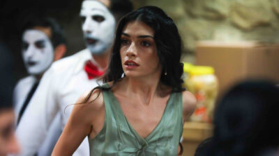 Hazar Erguclu como Cicek com vestido verde e expressao de susto durante cena da novela turca Chamas do Destino