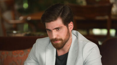 Berker Guven como Iskender Kayabeyli com blazer claro, barba e ferimentos no rosto em cena da novela Chamas do Destino