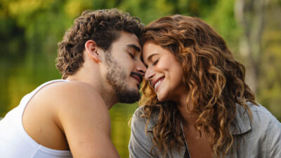 Filipe Bragança como João Raul e Isadora Cruz como Agrado encostam as testas com olhos fechados e sorrisos na novela Coração Acelerado sob luz solar