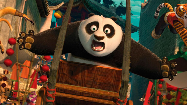 O panda Po com expressão de surpresa segura um carrinho de madeira durante cena de ação do filme Kung Fu Panda 2