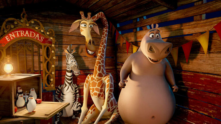 Personagens Marty, Melman, Glória e pinguins reunidos em cenário de circo de madeira em cena do filme Madagascar 3: Os Procurados