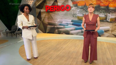 Maju Coutinho e Poliana Abritta apresentam o Fantástico em estúdio com telão exibindo seringas e a palavra "perigo"