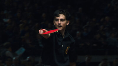 Timothée Chalamet como Marty Mauser segura raquete de pingue-pongue vermelha em cena de competição do filme Marty Supreme