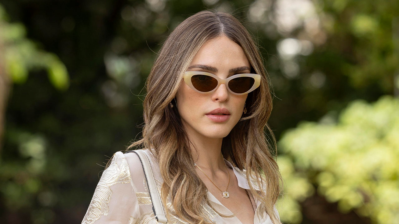 Isabelle Drummond vive Naiane Sampaio em Coração Acelerado. De óculos escuros e blusa bordada, ela posa séria em área verde