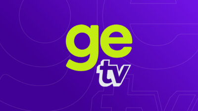 Logotipo da GE TV com as letras GE em verde limão e a sigla TV em branco com contorno azul inseridos em um fundo roxo vibrante estilizado