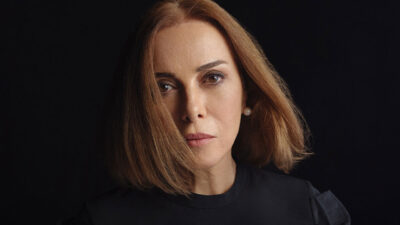 Zuhal Olcay como a personagem Tomris, com cabelo chanel, blusa preta e expressão séria em foto para a novela Chamas do Destino