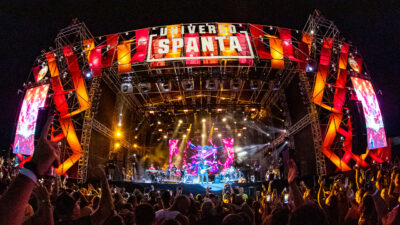 Palco do festival Universo Spanta no Rio de Janeiro com banda tocando sob luzes amarelas e estrutura vermelha para grande público em noite de show