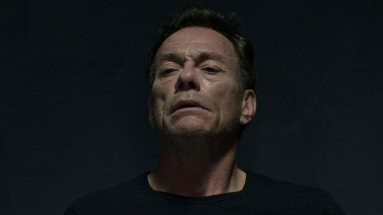 Jean-Claude Van Damme como Wheeler olha para o alto com expressão séria em fundo escuro no filme Black Water: Perigo no Oceano