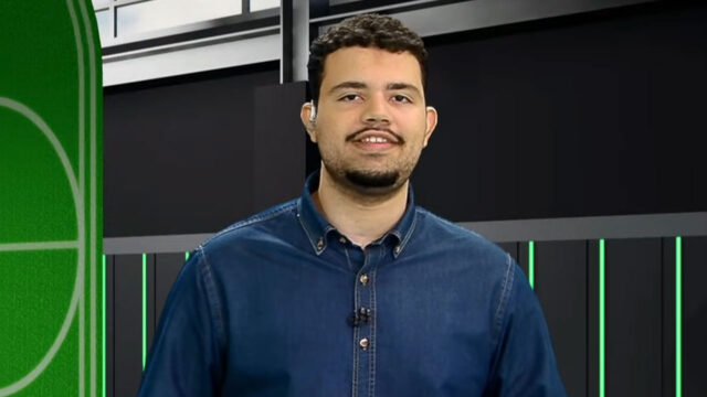 Zé Neto de camisa jeans sorri no estúdio da Xsports com elementos visuais que remetem a um campo de futebol ao fundo da imagem
