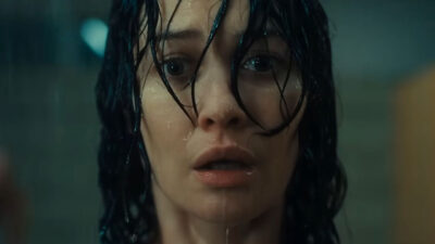 Olga Kurylenko interpreta Alice no filme Presença Maligna exibindo expressão de pavor com cabelos molhados e rosto úmido em plano detalhe sombrio