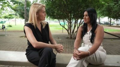 Ana Hickmann veste preto e entrevista Karine Maciel, de branco, sentadas em banco de praça arborizada para o programa Hoje em Dia da Record
