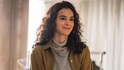 Bruna Marquezine como Bia na série Amor da Minha Vida, sorrindo levemente com cabelos cacheados soltos, vestindo jaqueta mostarda e blusa cinza
