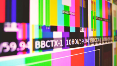 Barras coloridas de sinal de teste de TV com informações técnicas BBCTX-1 e 1080i 59.94 em destaque sobrepostas a padrões de calibração de broadcast