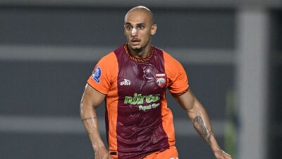 Leo Caxambu, jogador do Borneo FC, veste uniforme laranja e vinho com patrocínio Nitrea, possui curativo no nariz e tatuagens nos braços, em campo