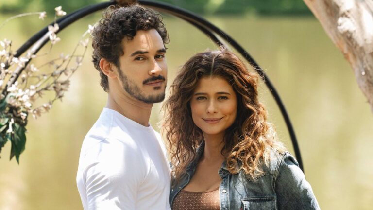 João Raul (Filipe Bragança) e Agrado (Isadora Cruz) posam juntos e sorridentes, ele veste camiseta branca e ela jaqueta jeans na novela Coração Acelerado