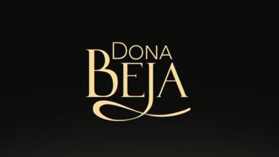 Logotipo da novela Dona Beja escrito em letras douradas e elegantes, com destaque para a letra B alongada, centralizado sobre um fundo preto fosco