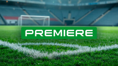 Logotipo do canal Premiere em letras brancas sobre retângulo verde centralizado em campo de futebol com gramado em destaque e trave ao fundo desfocada