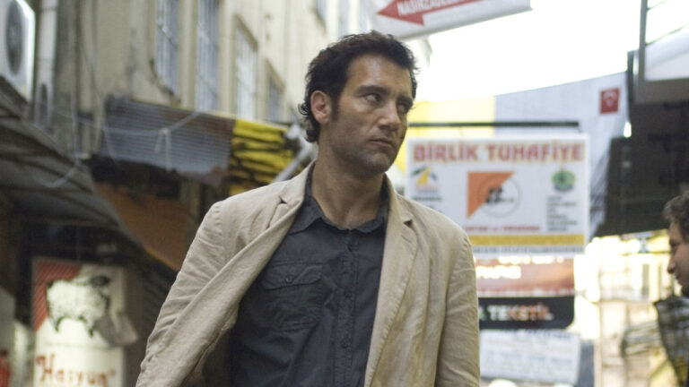 Louis Salinger interpretado por Clive Owen caminha por rua comercial olhando para o lado em cena do filme Trama Internacional