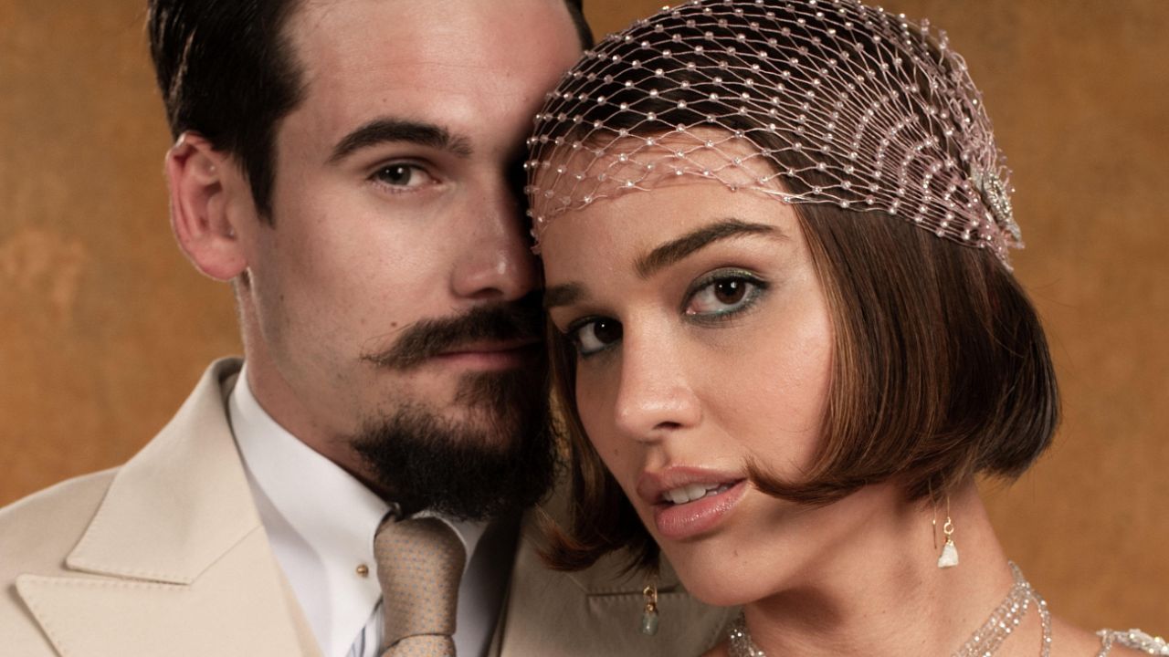 Nicolas Prattes como Mirinho e Theresa Fonseca como Virgínia em close, com roupas de gala dos anos 20 e acessório de brilho no cabelo da atriz