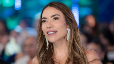 Patricia Abravanel sorri durante o Programa Silvio Santos usando brincos longos em estúdio iluminado com plateia desfocada ao fundo