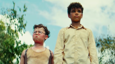 David McKenna como Piggy e Winston Sawyers como Ralph na série Lord of the Flies, Piggy usa óculos e regata e Ralph veste camisa bege, fundo com céu