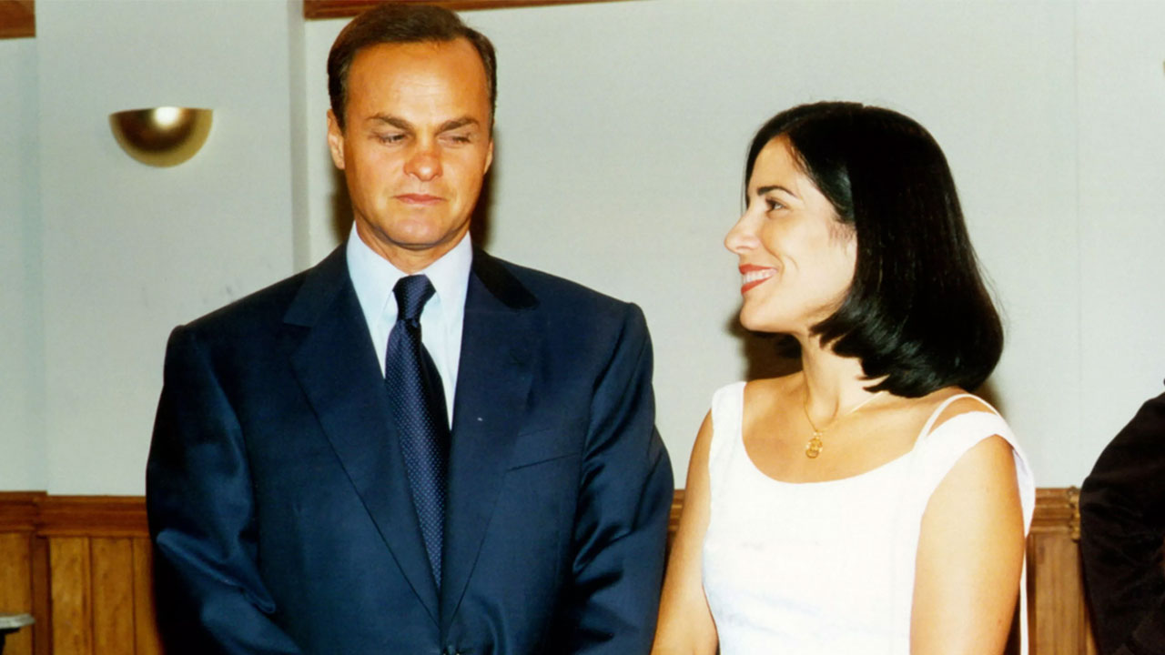 Kadu Moliterno como Rodrigo e Gloria Pires como Nice em cena da novela Anjo Mau, ele usa terno azul escuro e ela vestido branco com colar dourado