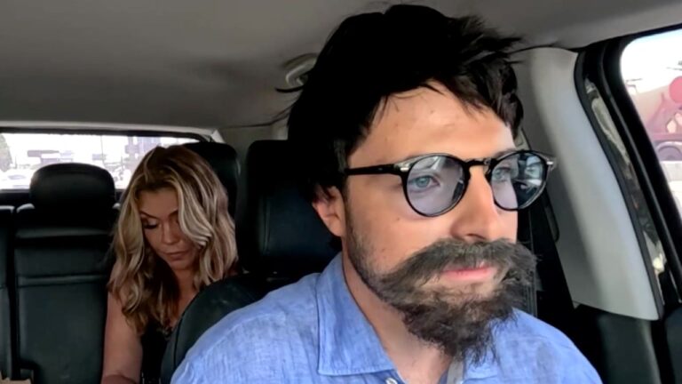 Simony e João Augusto sorriem dentro de um carro, ela ao volante de regata escura e ele no passageiro de camisa azul clara, usando óculos de sol redondos