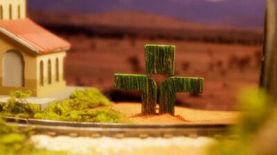 Maquete com prédio ao lado de trilhos de trem e símbolo verde da TV Cultura em cenário cenográfico