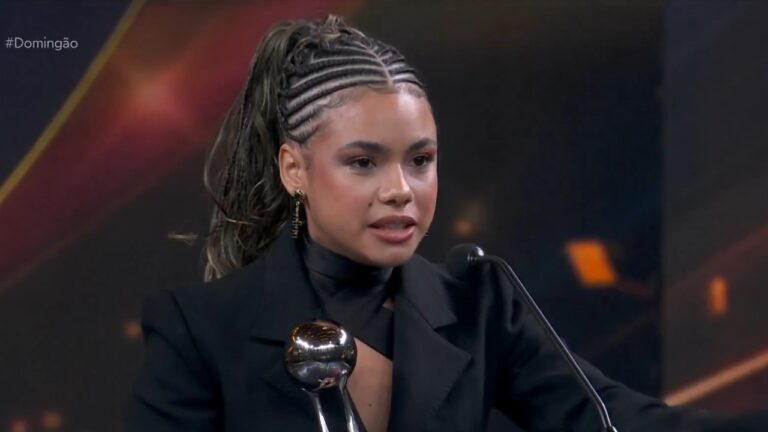 Alana Cabral discursa ao microfone ao receber prêmio no Melhores do Ano com troféu em destaque e hashtag Domingão na tela
