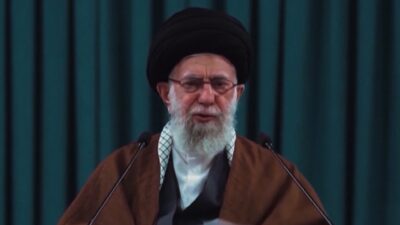 O ex-líder supremo do Irã, Ali Khamenei, discursa com semblante sério, ele usa turbante preto, óculos de grau e túnica marrom sobre traje cinza e branco