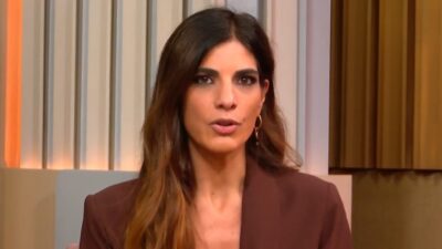 Jornalista Andréia Sadi fala no Estúdio I da GloboNews com blazer marrom em estúdio iluminado