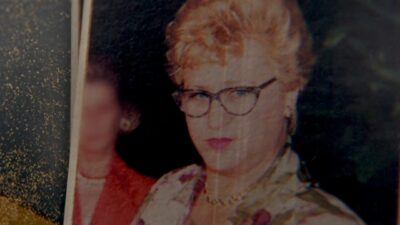 Anita Harley em foto antiga com cabelo curto loiro e óculos olha à frente com expressão séria em imagem com aspecto envelhecido e riscos visíveis
